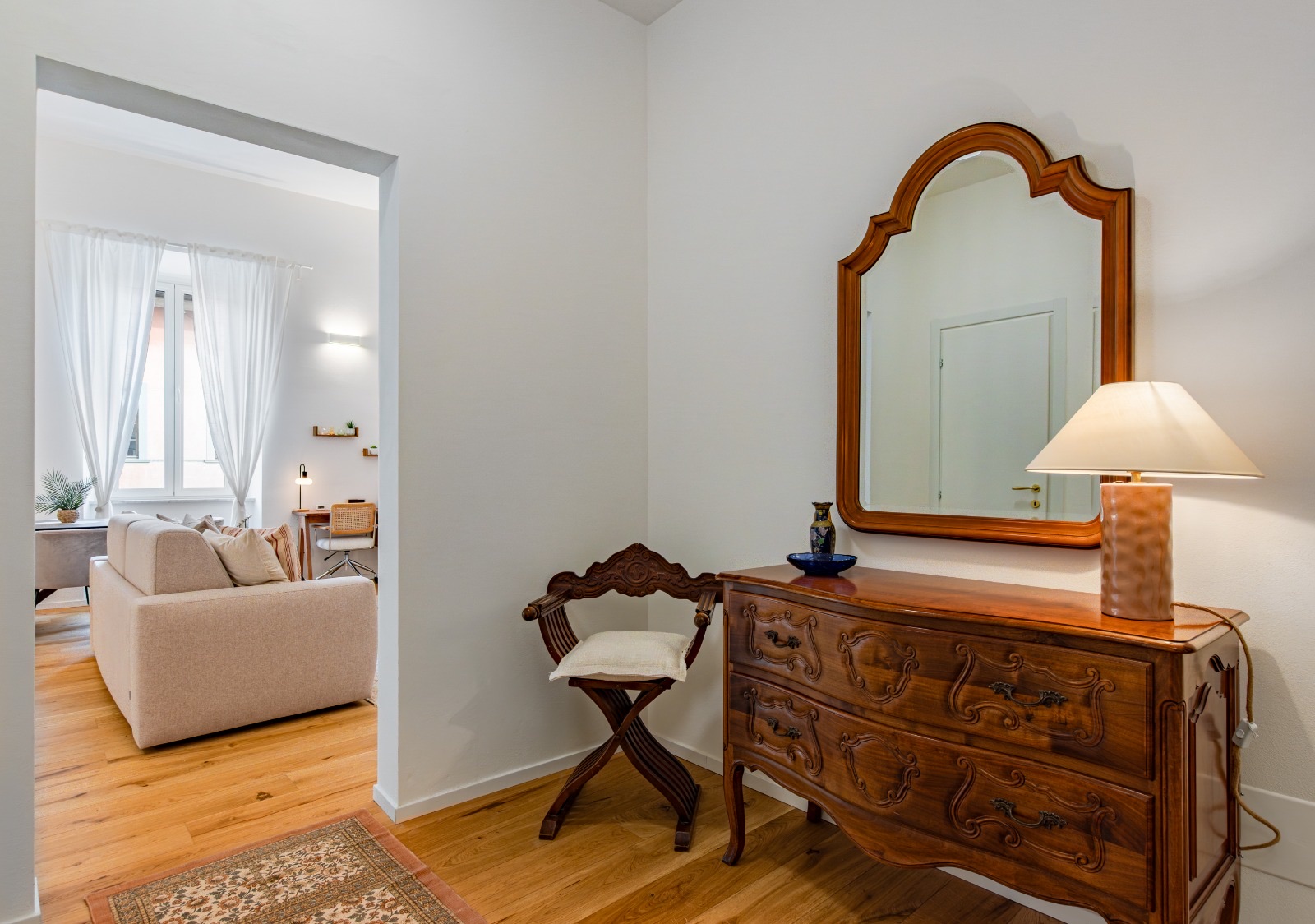 Entrance with an antique carved chest of drawers, framed mirror and table lamp