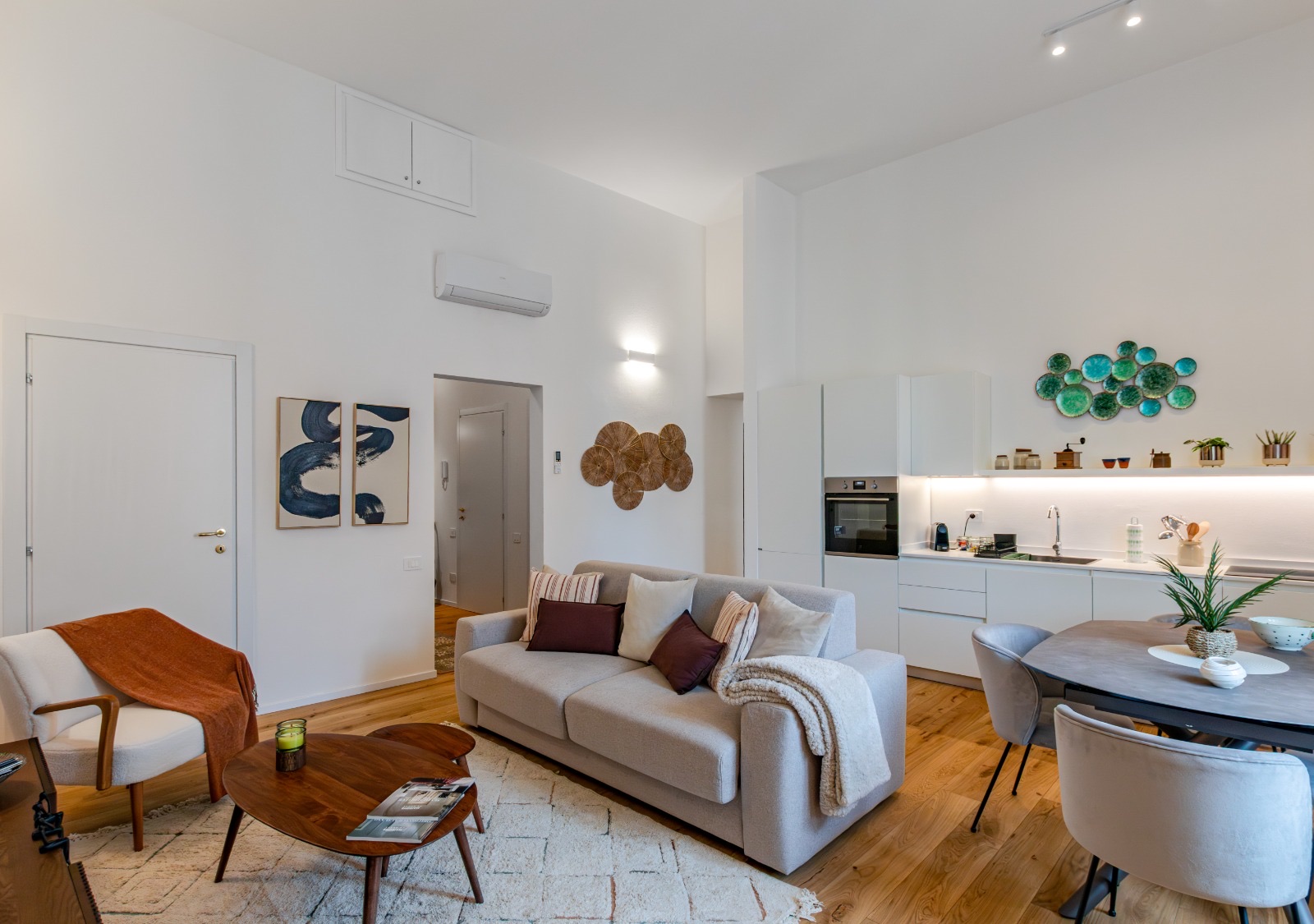 Living room with a grey sofa, armchair and wooden coffee tables, open white kitchen and dining table