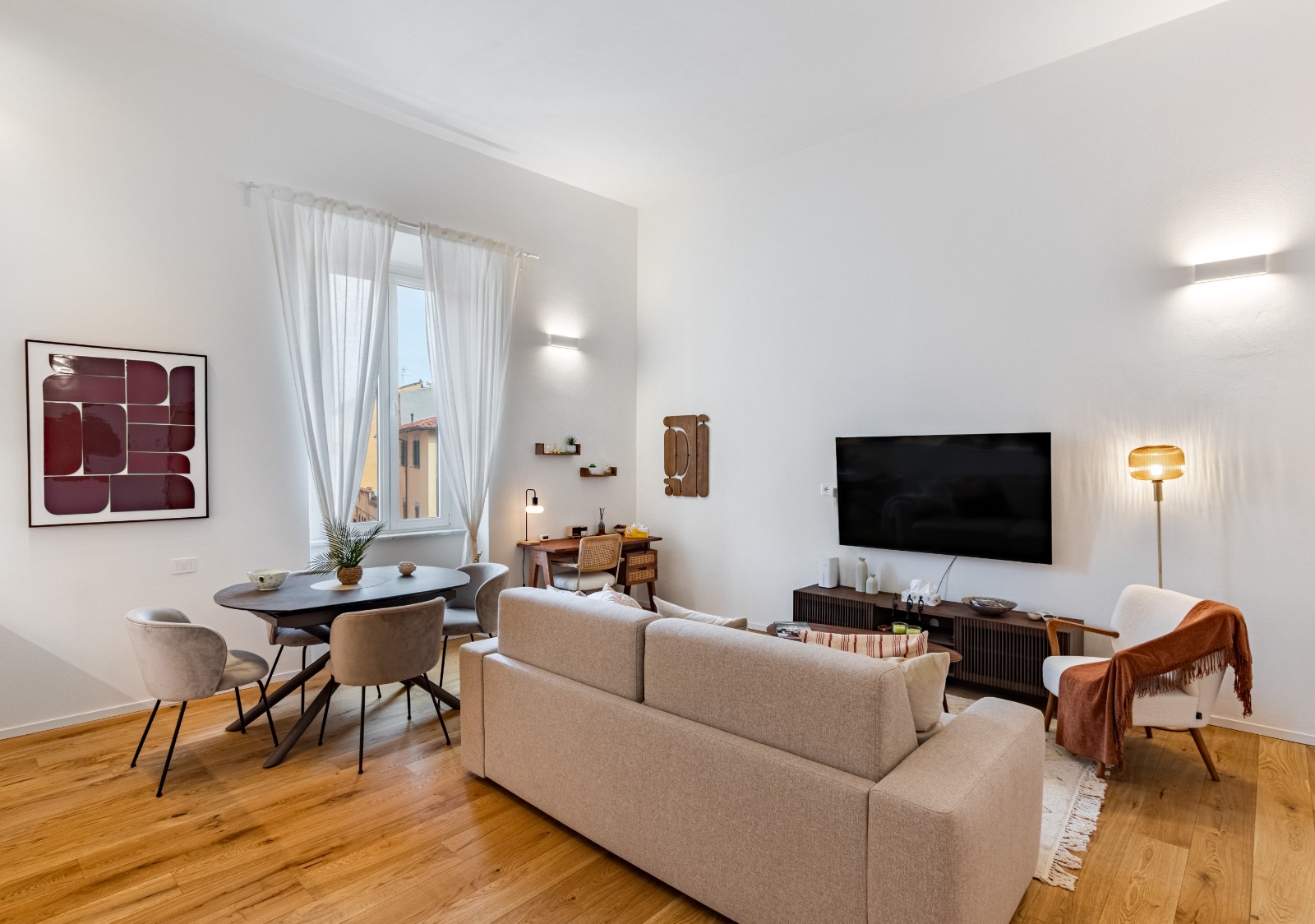 Living room with sofa, dining table by a tall window, desk and wall-mounted TV