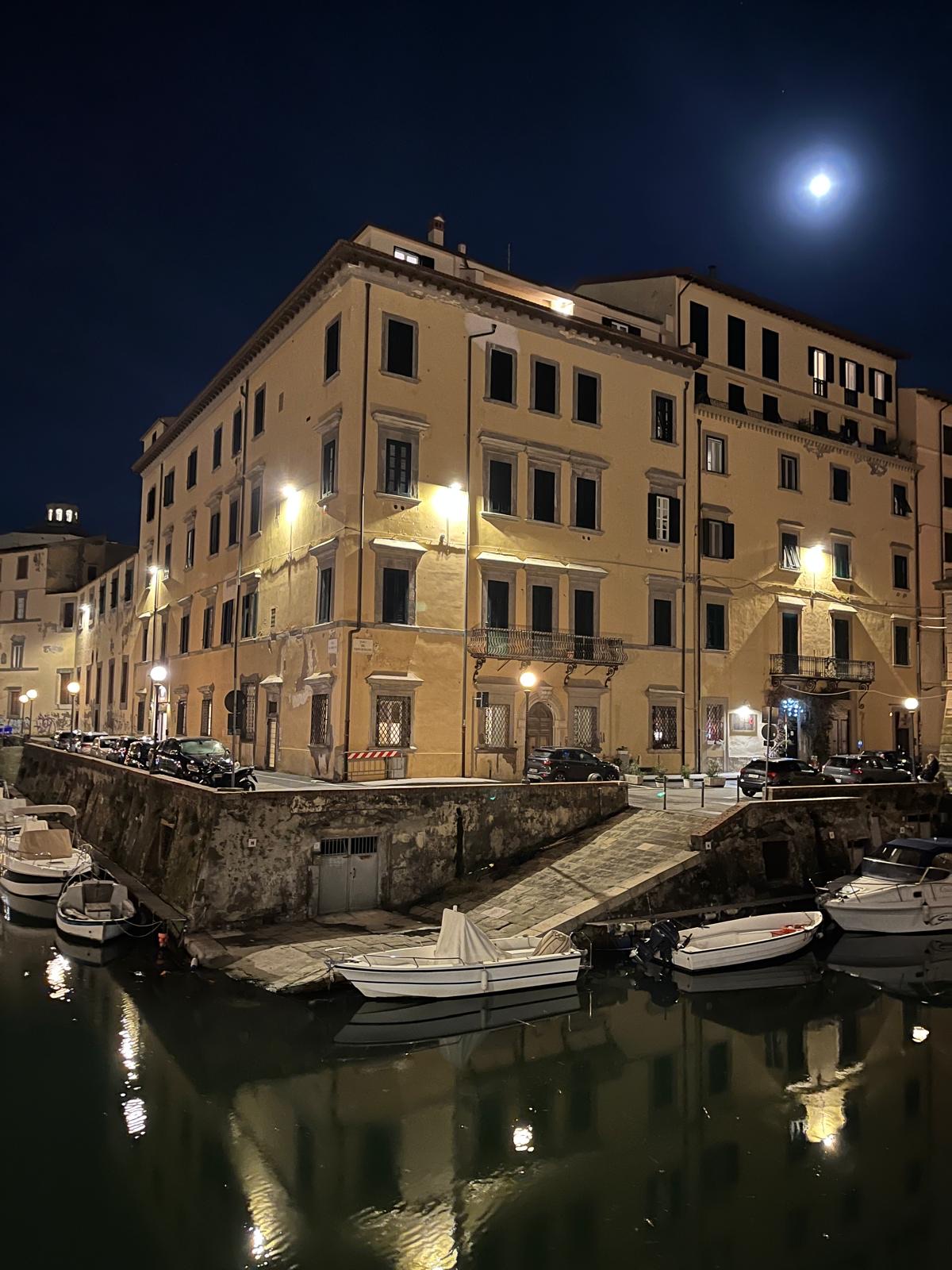 Venezia Nuova at night: a lit yellow palazzo, moored boats and the moon over the canal